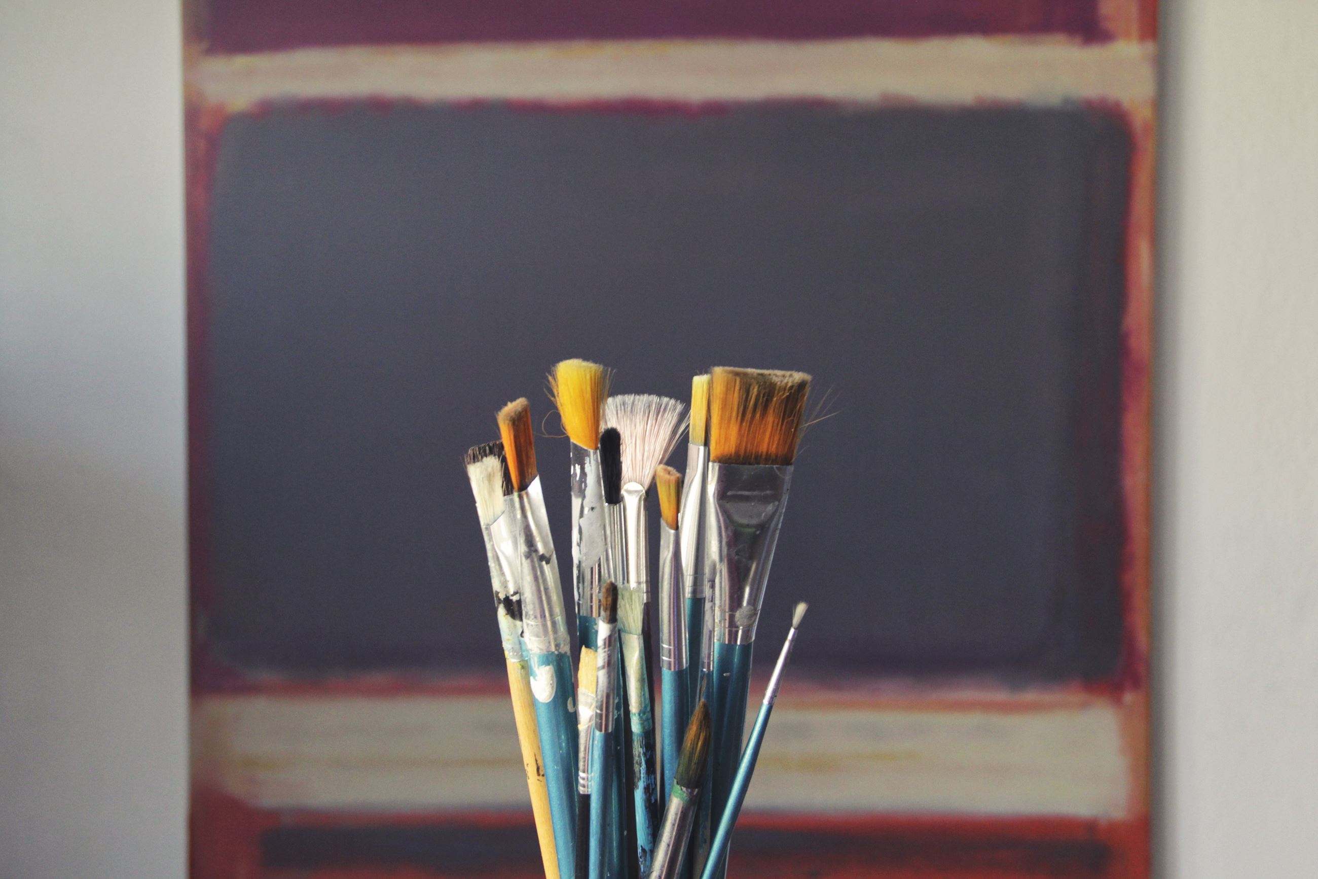 Photo of assorted paint brushes in front of a canvas.